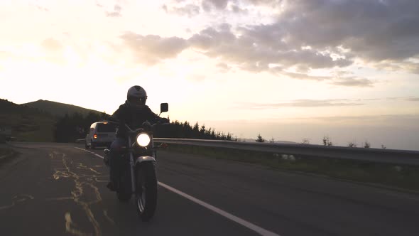 Silhouette of Biker Riding Motorcycle on Mountain Road Passing Cars Going in Opposite Direction at