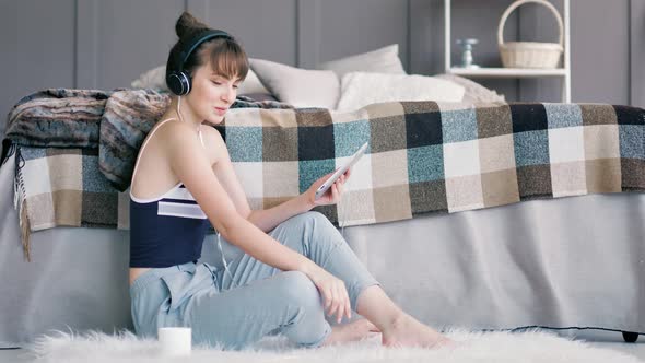 Young Cheerful Teenager Woman Enjoying Music in Headphones Using Tablet PC at Home Interior