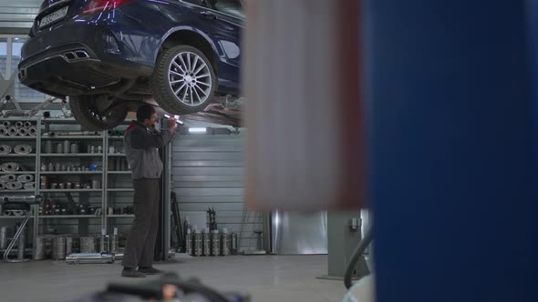 General Plan The Mechanic Inspects the Exhaust System of the Car in the Car Service
