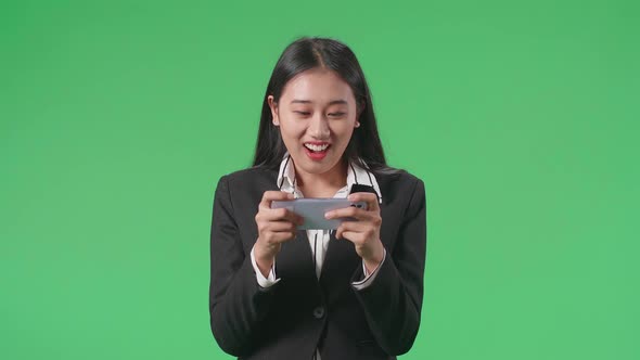 A Smiling Asian Business Woman Using Mobile Phone Playing Game In The Green Screen Studio