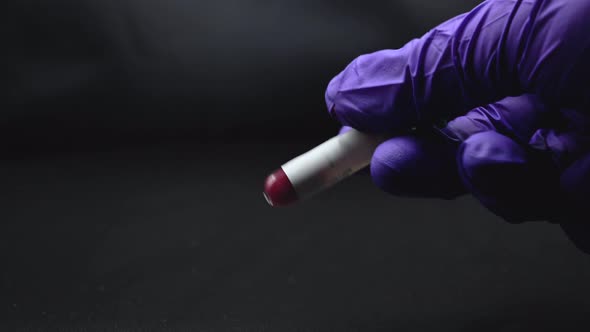Gloved Hand Shaking Test Tube of Blood on Blackbackground.