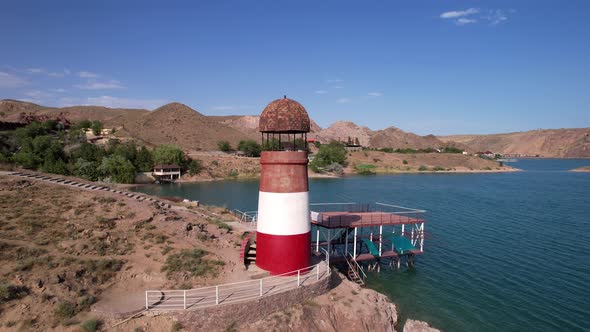 White and Red Lighthouse on the Shore of the Lake