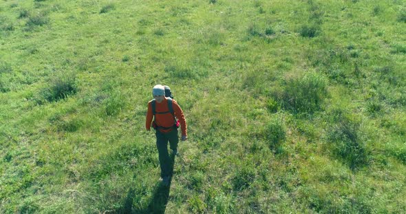 Flight Over Backpack Hiking Tourist Walking Across Green Mountain Field. Huge Rural Valley at Summer