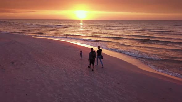 Young Family Walking With a Child on a Beach at Sunset.