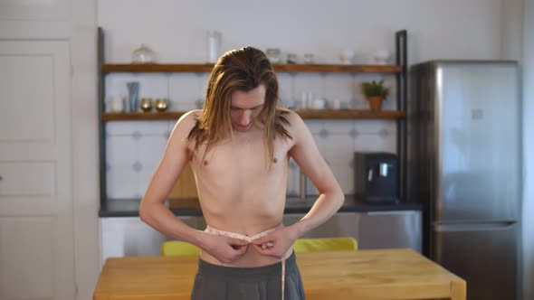 Young Thin Shirtless Man Measuring Waist with Tape at Home