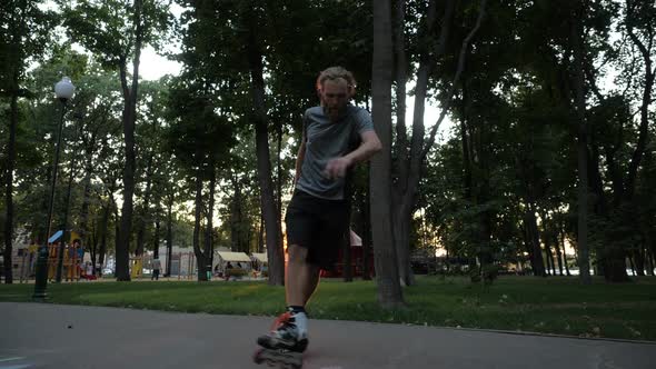 Young Long-haired Bearded Man Roller Skater Is Dancing in a Nice Evening in a City Park. Freestyle