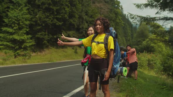 Cheerful Lovely Multiethnic Women Travelers Hitchhiking on Mountain Road