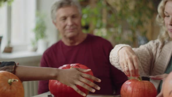 Old Lady Sitting at the Table and Showing a Young Girl a Pumpkin for Halloween