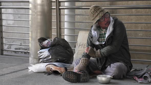 Homeless old man in dirty clothes sitting on the street and asking for help