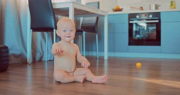 Little Naked Blond Babe is Sitting on the Floor in an Apartment and is Looking at the Camera