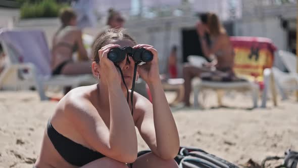 Beautiful Girl Looks Through Binoculars on the Beach