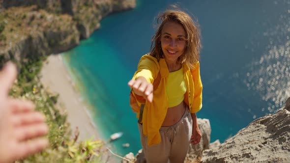 POV Happy Woman Hiker in Yellow Shirt Gives Hand to Her Teammate on Edge of Cliff on Mountain Top