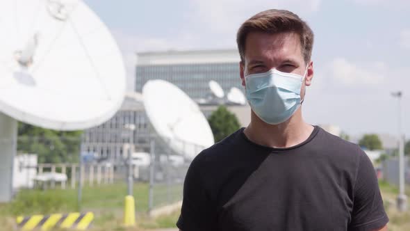 A Young Handsome Man in a Face Mask Shows a Thumb Up To the Camera and Nods in an Urban Area