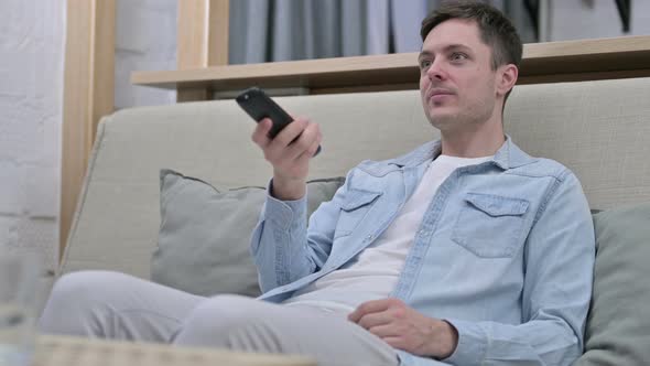 Attractive Young Man Sitting on Sofa and Watching TV 