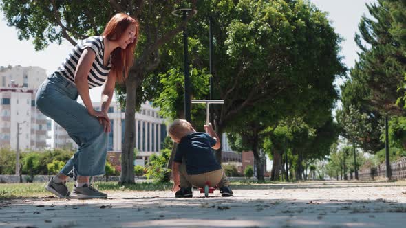 A Little Boy Picks Up a Scooter From the Ground and Goes for a Walk with His Mother