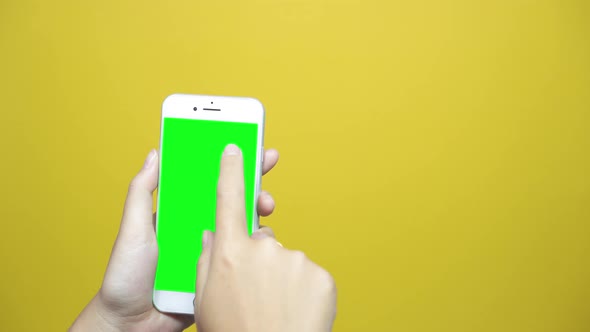 Woman using smart phone with green screen on yellow table background.