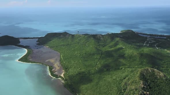 Drone shoots an island with hills and a serpentine road, around the azure sea at Antigua and Barbuda