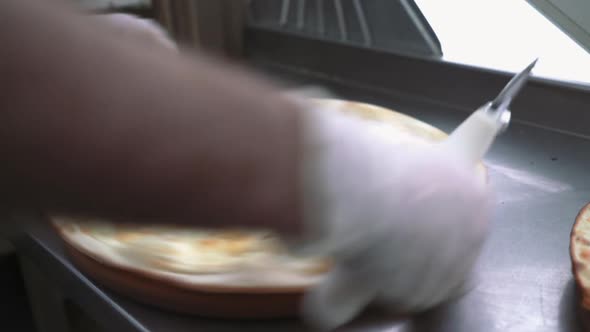 Cutting pizza on slices with special knife. Hand holding knife.