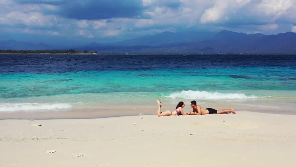 Two people sunbathe on perfect bay beach wildlife by shallow sea and white sand background of Bali a