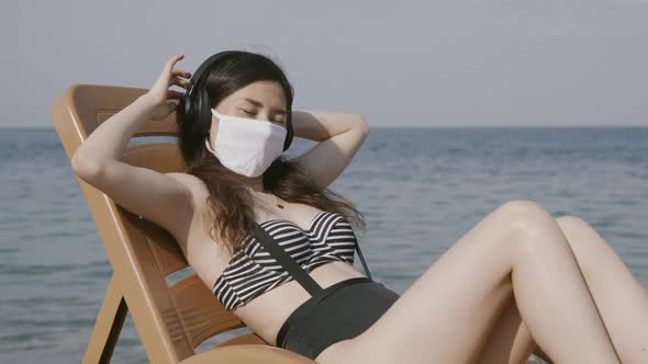 Young Woman in Medical Mask Relaxing on Beach Deck Chair By the Sea with Eyes Closed Wearing