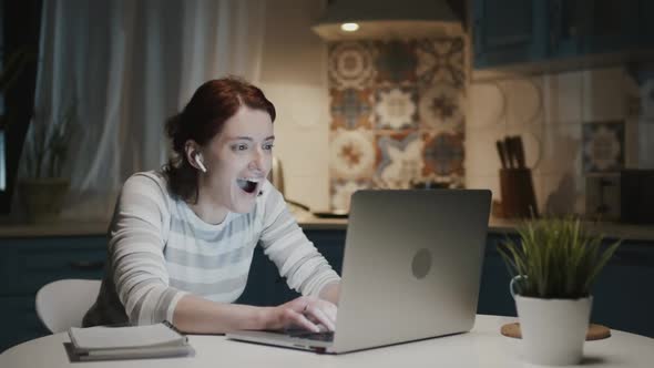 Woman In The Kitchen With Laptop. Something Surprises Her And She Smiles