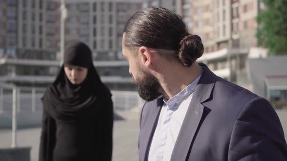 Close-up Face of Angry Middle Eastern Man Looking Back at Blurred Muslim Woman in Traditional Hijab