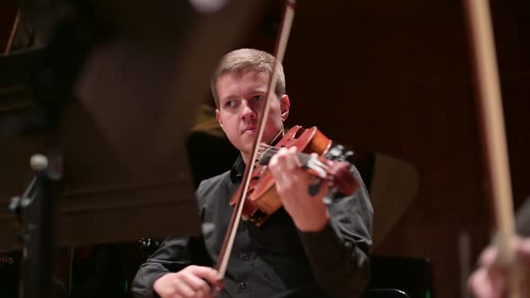 Young male violinist playing the violin to the accompaniment of the orchestra