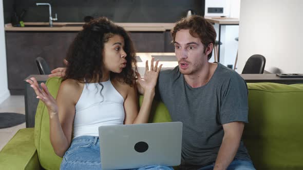 Mixed Couple Quarreling While Using Laptop While Sitting on Sofa at Home. Family Conflict