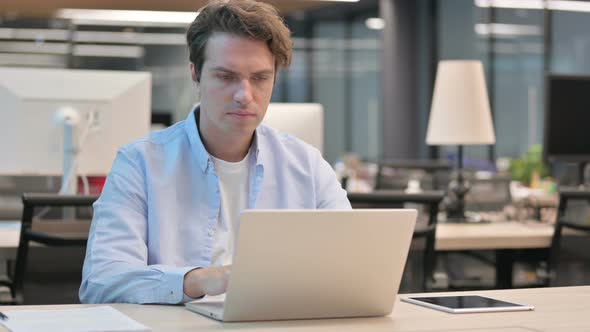 Man Pointing at Camera While Using Laptop in Office