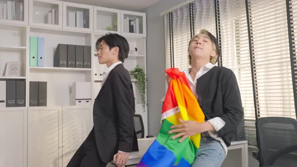 Asian businessman gay dancing in office workplace and hold LGBTQ flag. Homosexual-LGBTQ concept