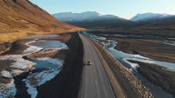 Car of Empty Road in Wilderness of Iceland Passing by Glacial Creek and Volcanic Mountains on Sunny