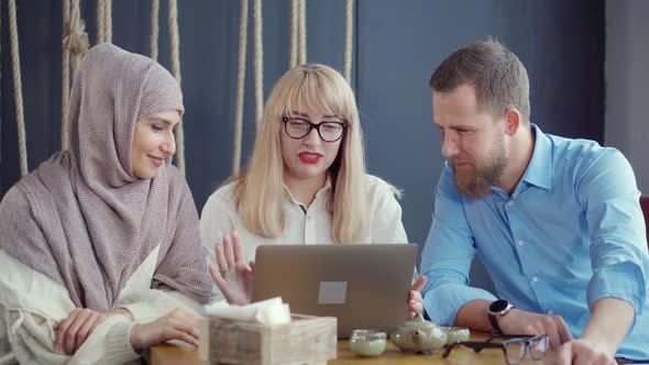 Arab Woman and Caucasian Pair Are Talking and Watching on Laptop in Cafe