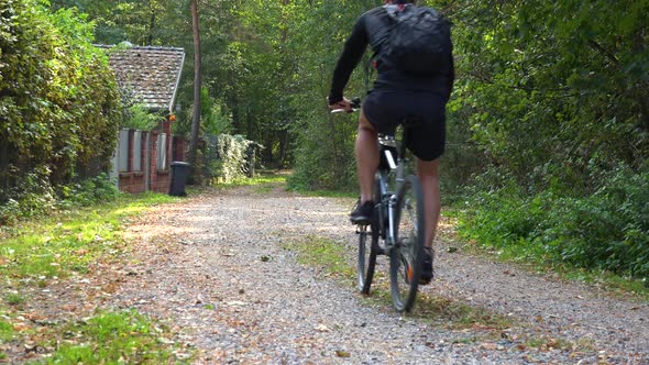 A Cyclist Rides Down a Path Through a Rural Area - Rear View