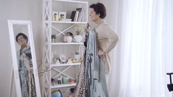 Side View of Happy Middleaged Woman Standing in Front of Mirror at Home Admiring New Dresses