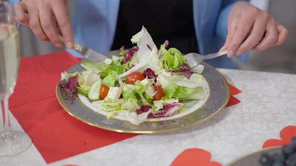 Closeup of Greek Salad in Plate with Female Hands Using Fork and Knife Mixing Ingredients