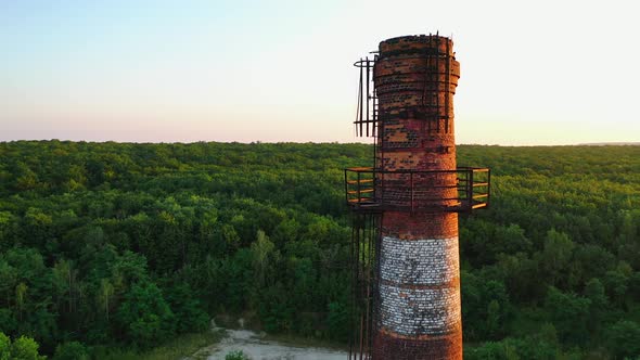 Brick industrial tower on nature background. Old pipe in ruined plant at sunset.