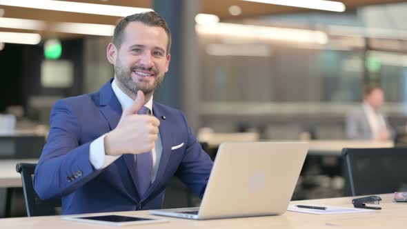 Thumbs Up By Middle Aged Businessman with Laptop at Work