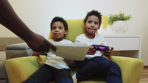 Two Little Black Boys Brothers Playing Game and Their Parent Brings Their Homework Instead of