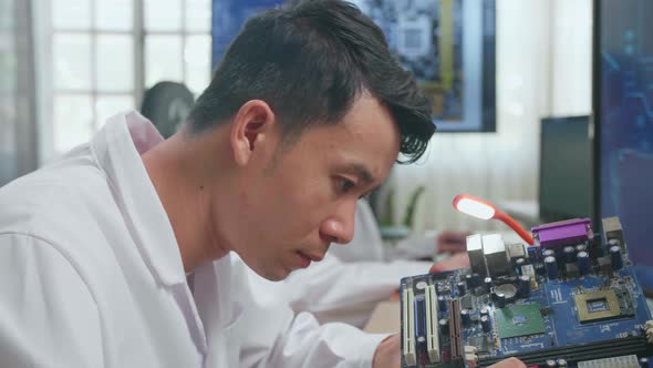 Asian Male Engineer Inspects Printed Circuit Board Motherboard. Scientist Designs Industrial Pcb