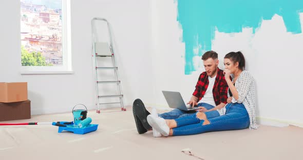 Portrait of Cute Cheerful Caucasian Family Wife and Husband Tapping on Laptop Looking for Decoration