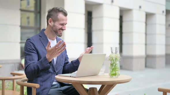 Man Celebrating While Using Laptop Sitting in Outdoor Cafe on Bench
