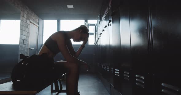 Sad Sporty Caucasian Woman Sitting Alone in Dark Gym Locker Room Feeling Lost and Upset Overcoming