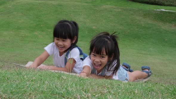 Two smiling little sisters lie prone on cardboard boxes sliding down