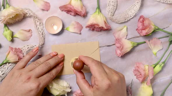 Hands sealing melted wax on an envelope near pink flowers