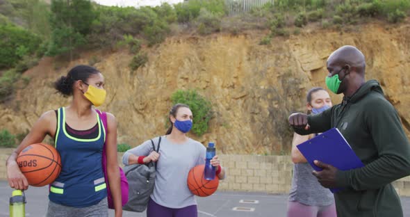 Diverse female basketball team and male coach wearing face masks greeting with elbows