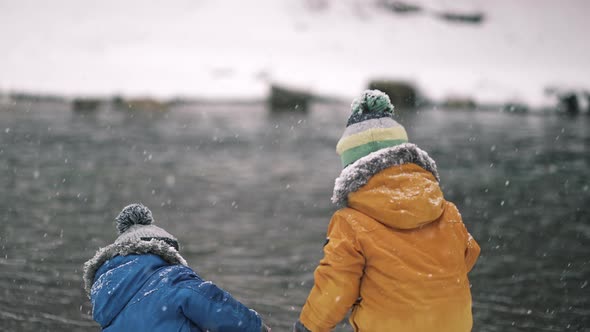 Little Twins Boys Playing with Snow Near River at Winter