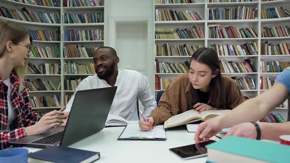 Smiling Multiracial Youth which Working Together Over their University Task in Reading Room