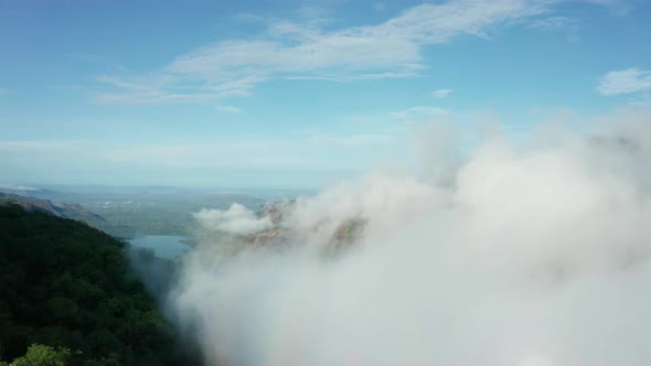 Forward drone shot through fog clouds, over forest mountains towards a distant lake of Western Ghats