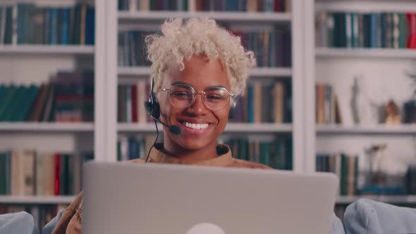 Positive African American Female in Headset Sit By Laptop Waving Hand to Camera