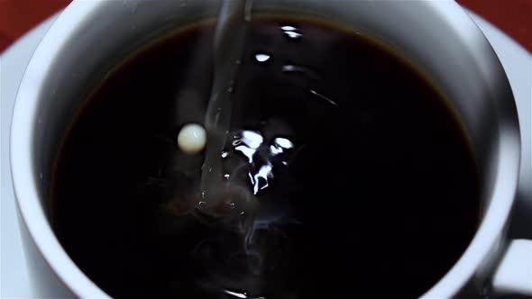 In Cup of Black Coffee Poured Milk. Top View. Closeup